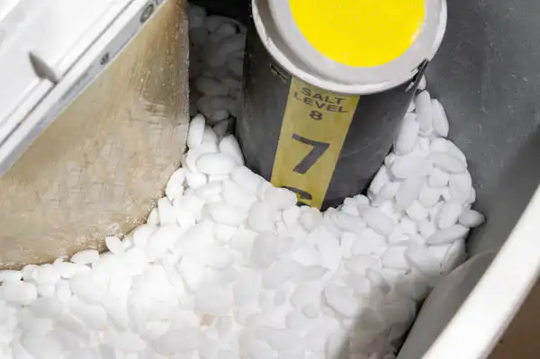A water softener tank filled with white salt pellets and a labeled yellow salt level indicator.